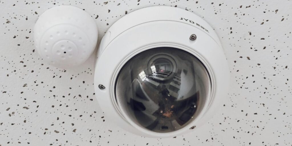 Close-up of a round dome surveillance camera installed on a speckled ceiling for security monitoring.