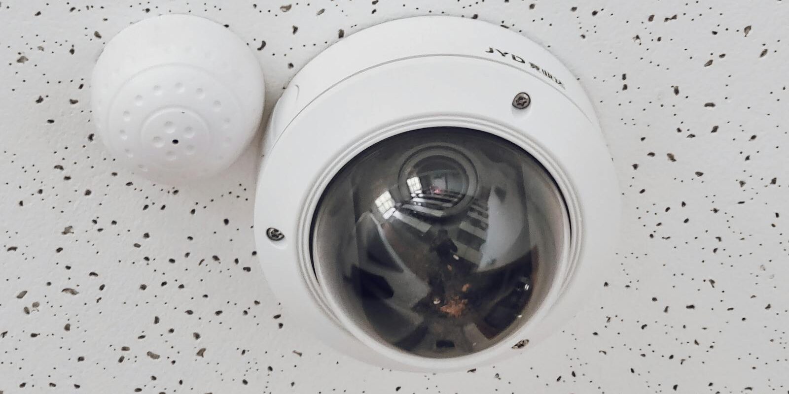Close-up of a round dome surveillance camera installed on a speckled ceiling for security monitoring.